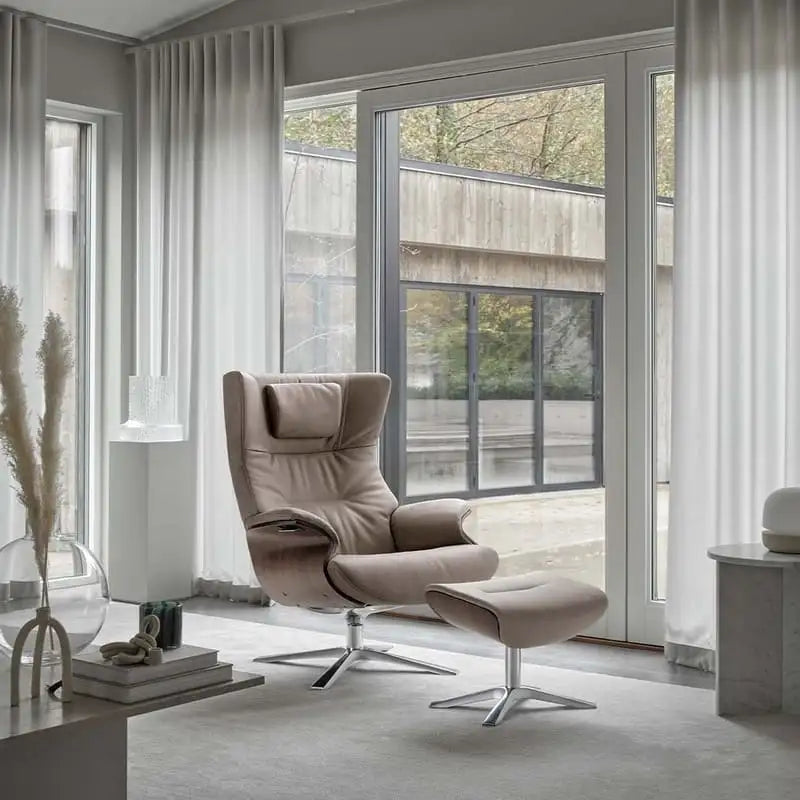 Beige Ledersessel mit passendem Hocker und chromem Sternfuß.