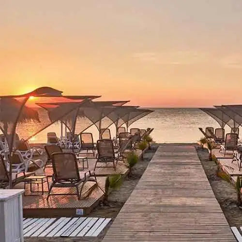 Holzsteg mit Liegestühlen und Sonnenschirmen am Strand bei Sonnenuntergang.